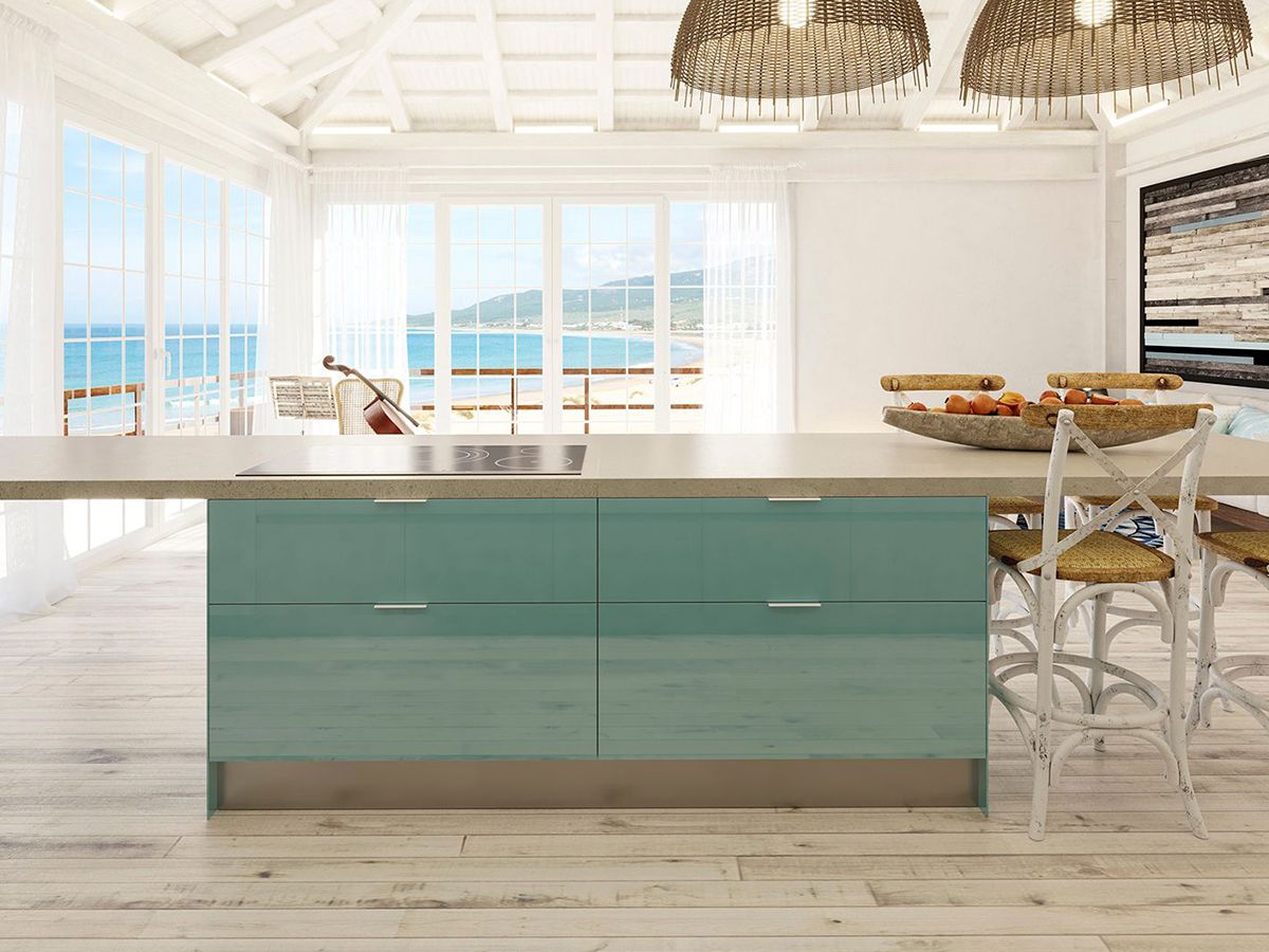 Ilha de cozinha lacada a azul turquesa, situada numa casa de praia com chão de madeira, com a praia ao fundo num dia de sol.
