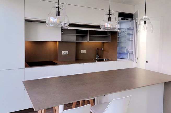 Cozinha de cor clara com ilha com bancada em cerâmica Laminan e luminárias suspensas naturais