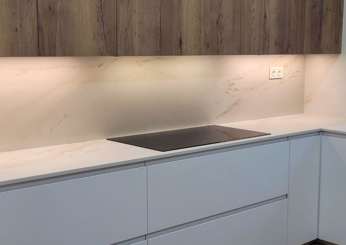 Pormenor da bancada branca com placa vitrocerâmica preta sobre armários brancos e com iluminação na base dos armários superiores.