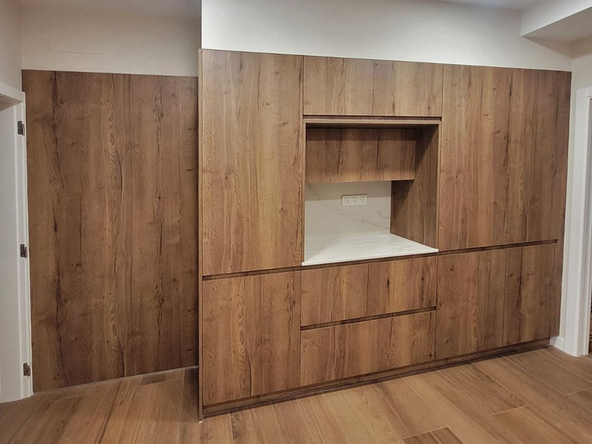 Vista frontal de um móvel de cozinha embutido em madeira com um nicho no meio.