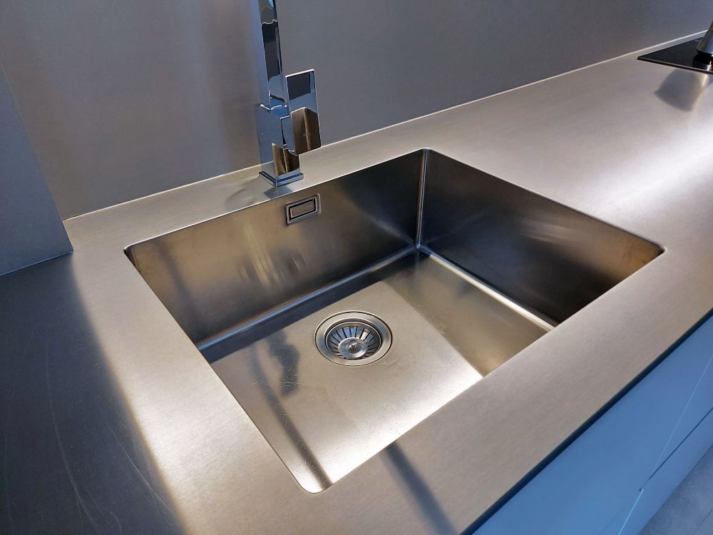 Detalhe do lava-loiça integrado na bancada de aço inoxidável maciço com torneira prateada