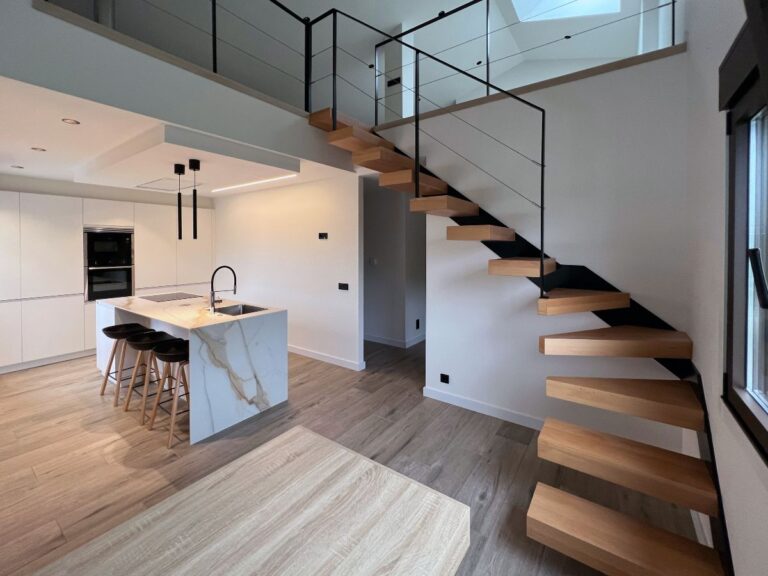 Cozinha branca moderna com ilha aberta para a sala de estar ligada às escadas que conduzem ao piso superior.