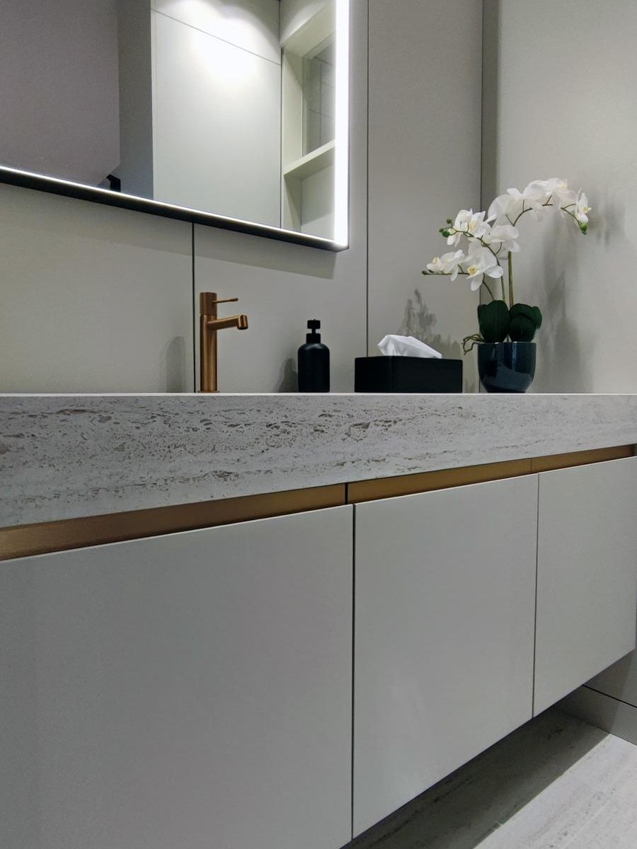 Pormenor do móvel Fussion da Senssia numa casa de banho moderna, com puxadores de cobre personalizados, torneiras a condizer e bancada com lavatório Dekton em mármore integrado.