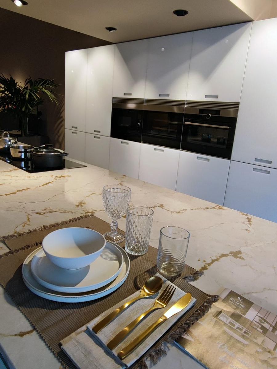 Pormenor da cozinha modelo Aral by Senssia com ilha suspensa em vidro lacado branco mate, bancada em Silestone Ivory Versailles e colunas equipadas com electrodomésticos integrados.