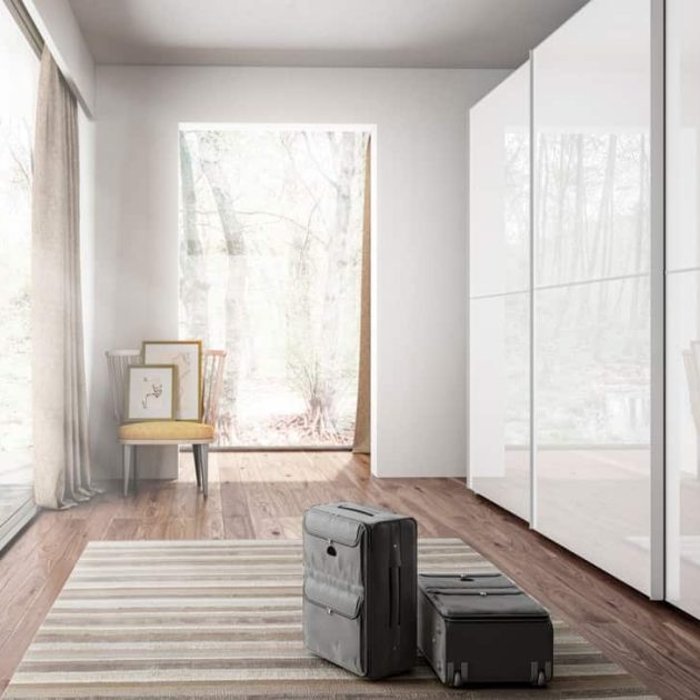 Vista lateral de armario amplio en color blanco de aluminio y cristal en habitación luminosa